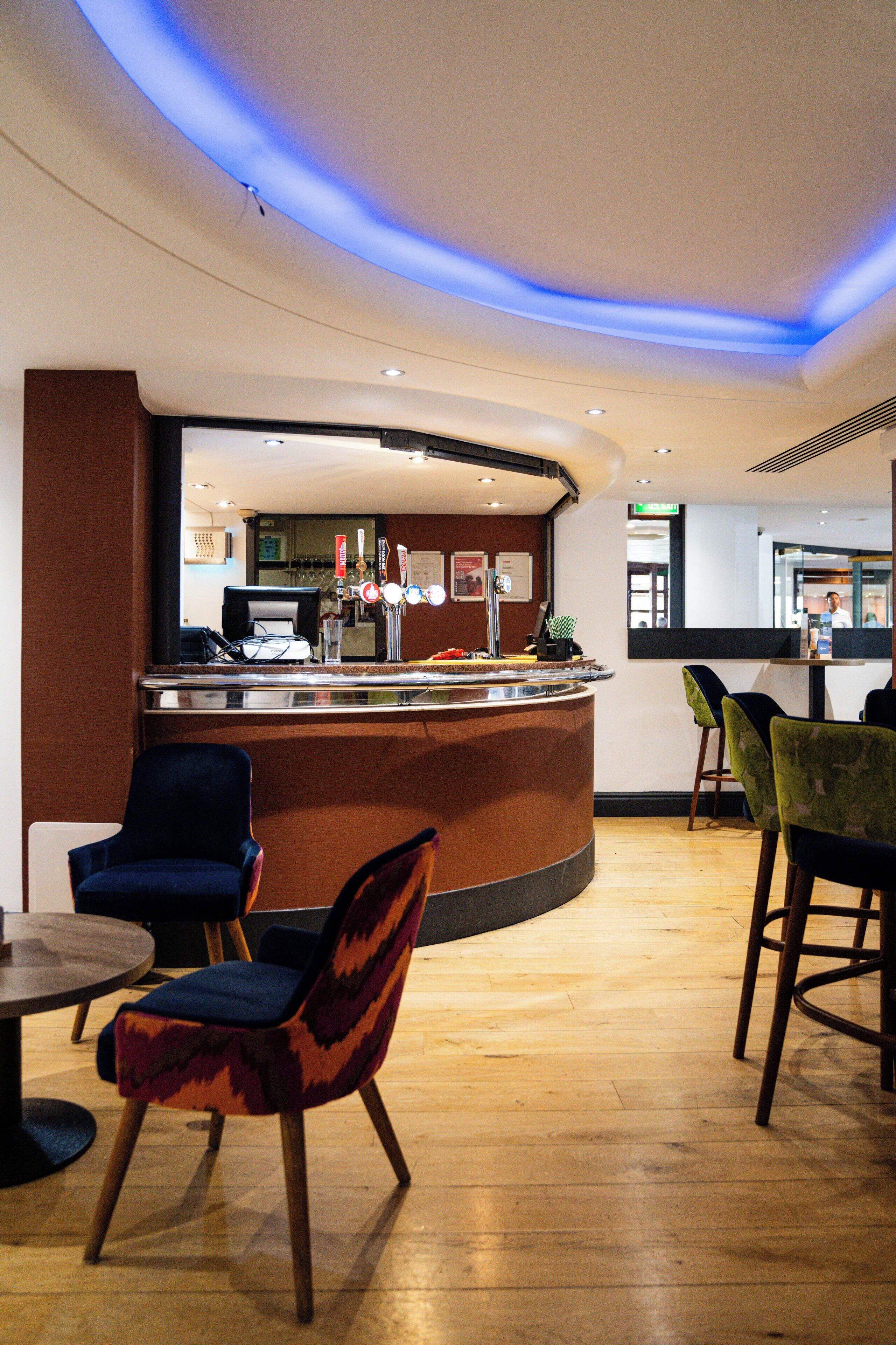 A hotel lobby with a curved reception desk, bar area, and seating with chairs and tables.
