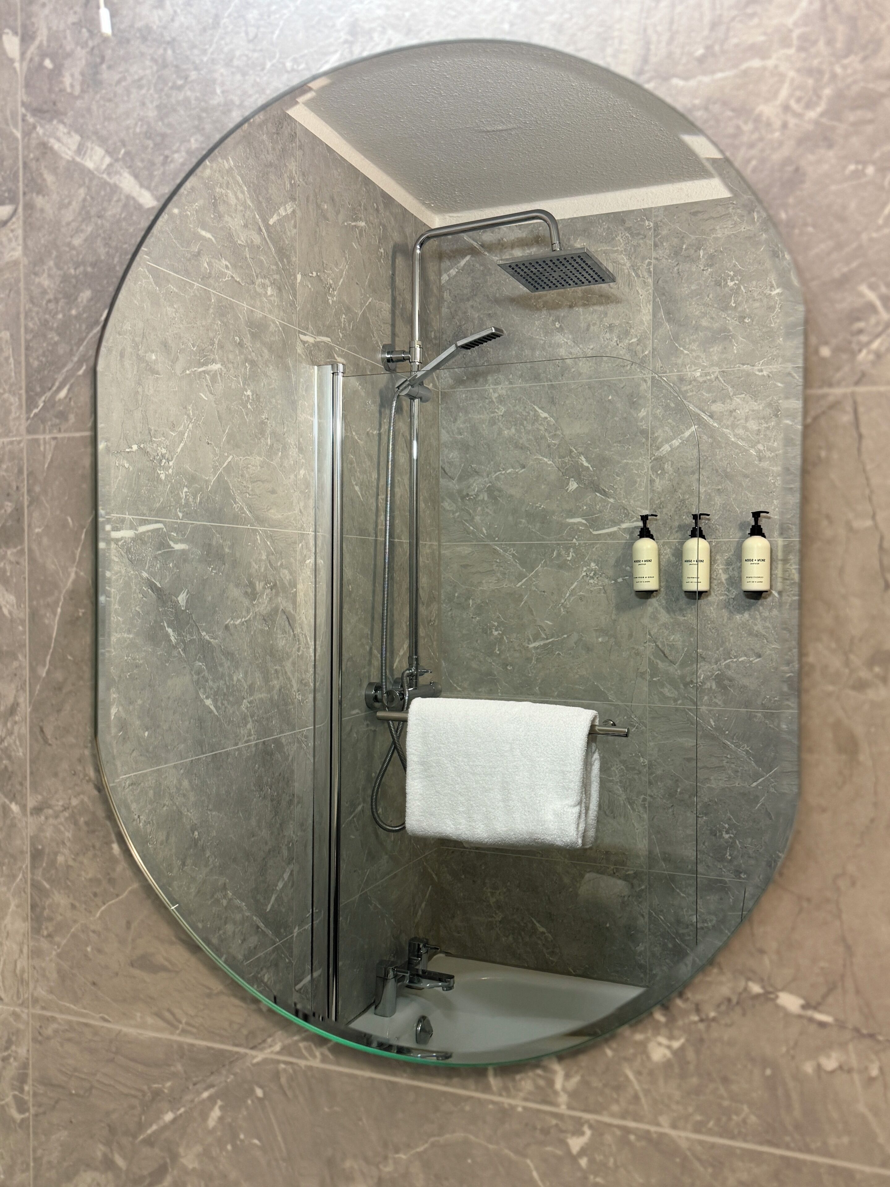 A bathroom with a glass-enclosed shower, a white towel, and three bottles of shampoo.