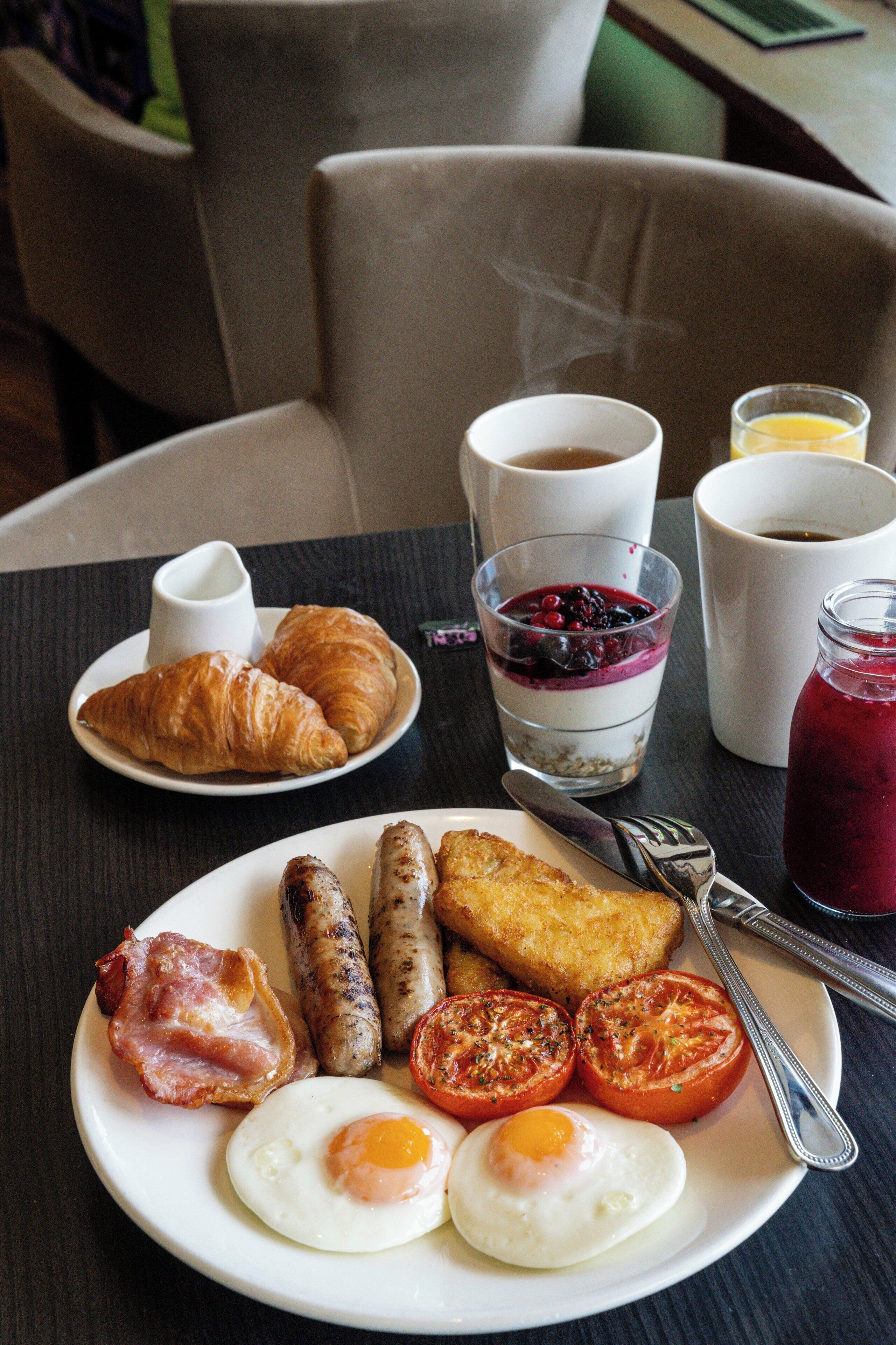 Un plato de desayuno con huevos, salchichas, tocino, tomates y croissants.