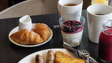 A breakfast plate with eggs, sausages, bacon, tomatoes, and croissants.