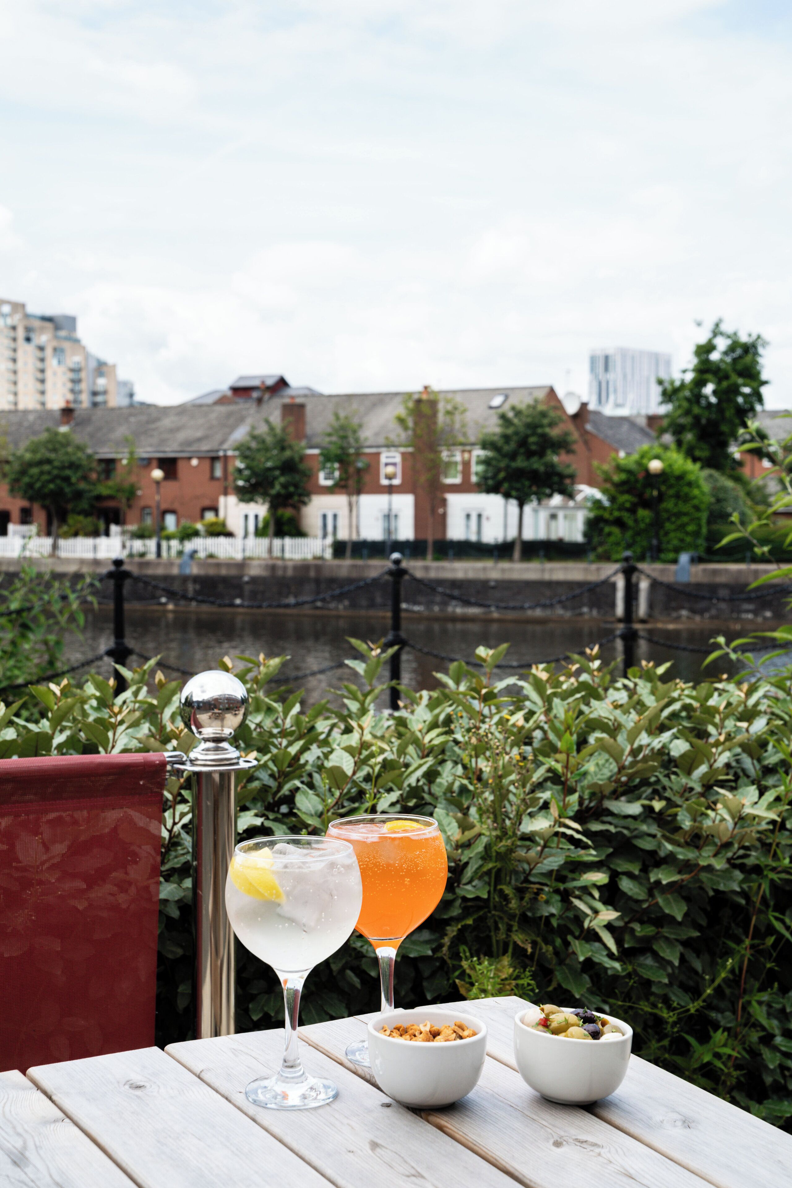 A table with drinks and bowls of nuts, set against a backdrop of greenery and buildings.