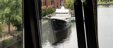 A view from a window overlooking a river with a boat, a red brick building, and a modern building across the water.