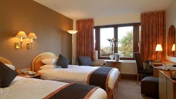 Habitación de hotel con dos camas, un escritorio, una silla, ventana con cortinas y lámparas fijadas a la pared.