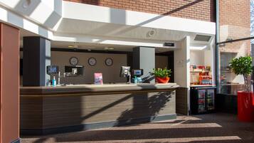 A reception area with a counter, clocks, a plant, and a vending machine.