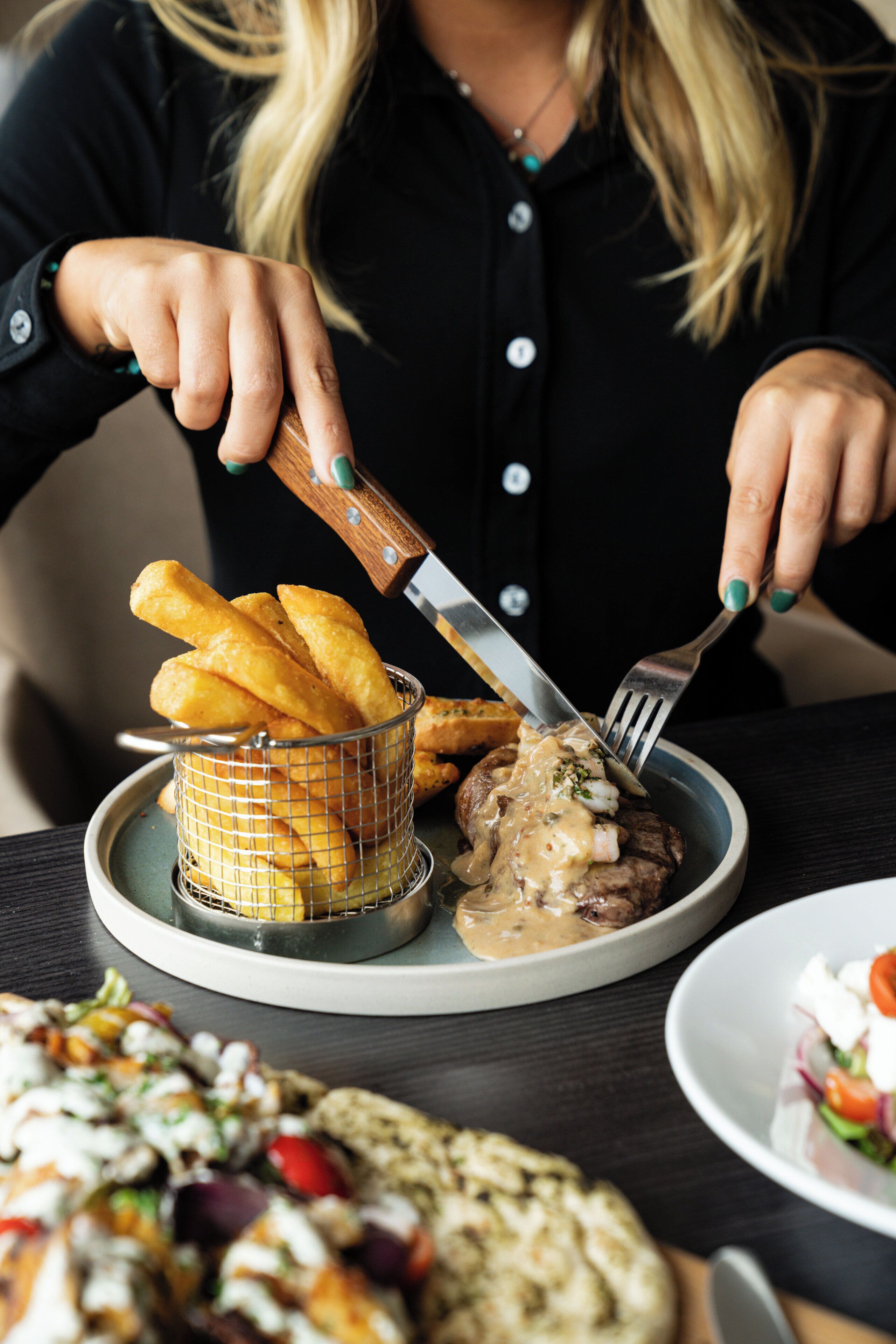 A person dining with a plate of food including breadsticks, a meat dish with sauce, and a salad.