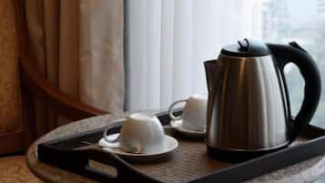 Una bandeja con un hervidor de acero inoxidable, dos tazas blancas y un platillo sobre una superficie texturizada, cerca de una ventana con cortinas.