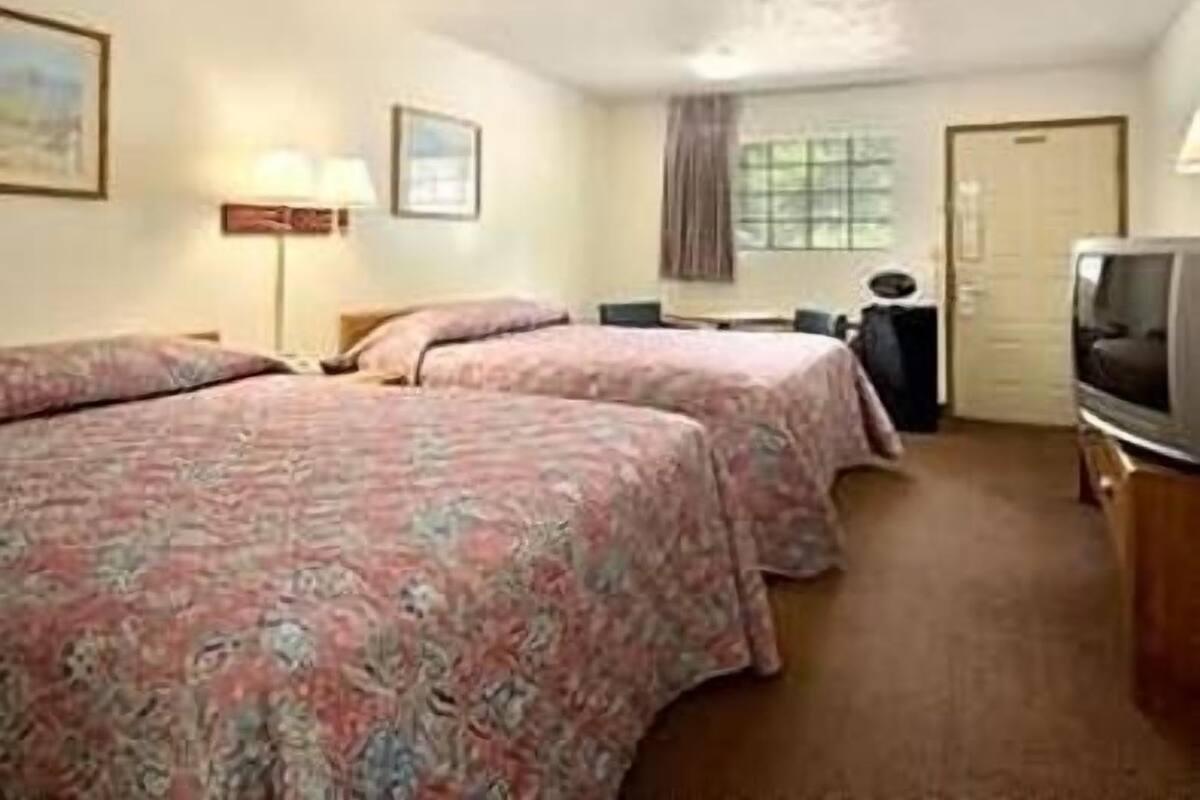 A hotel room with two beds, a desk, a chair, a television, and a window with curtains.