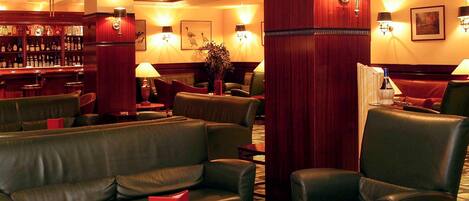 A bar area with leather seating, a red table, and a bookshelf with liquor bottles.