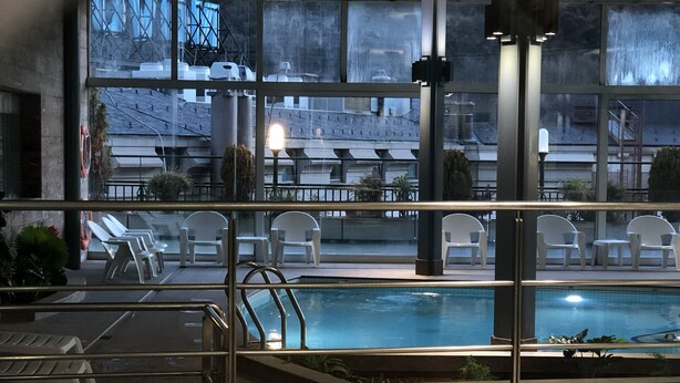 An indoor swimming pool with a hot tub, lounge chairs, and a view of the cityscape through large windows. - Mercure Andorra (Andorra la Vella)