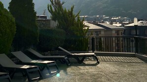 A terrace with lounge chairs, a stone wall, and a view of distant mountains and a town. - Mercure Andorra (Andorra la Vella)