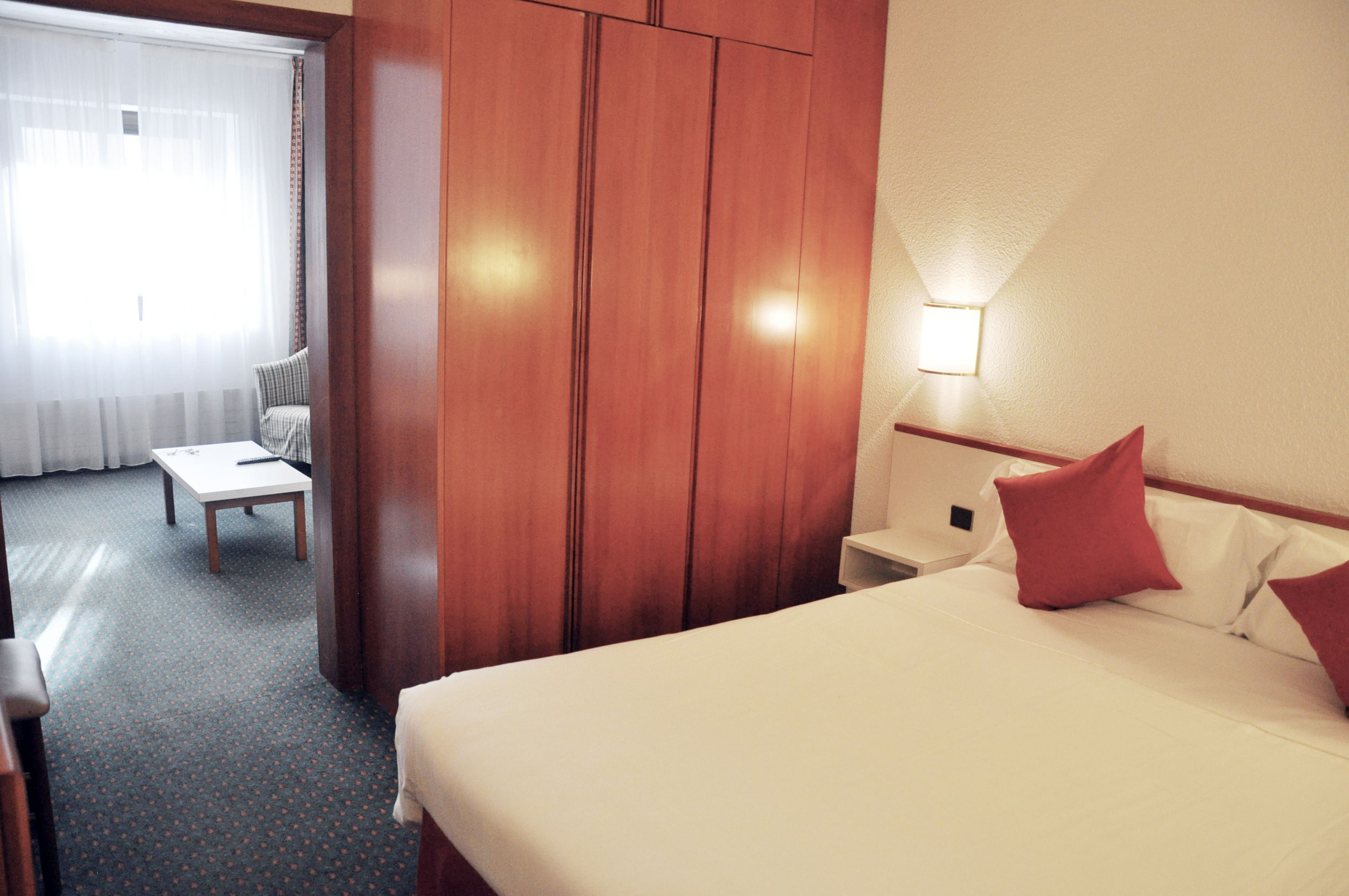 Una habitación de hotel con cama, mesita de noche, una silla y un armario de madera.