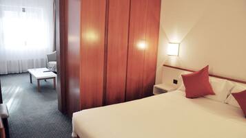Una habitación de hotel con cama, mesita de noche, una silla y un armario de madera.
