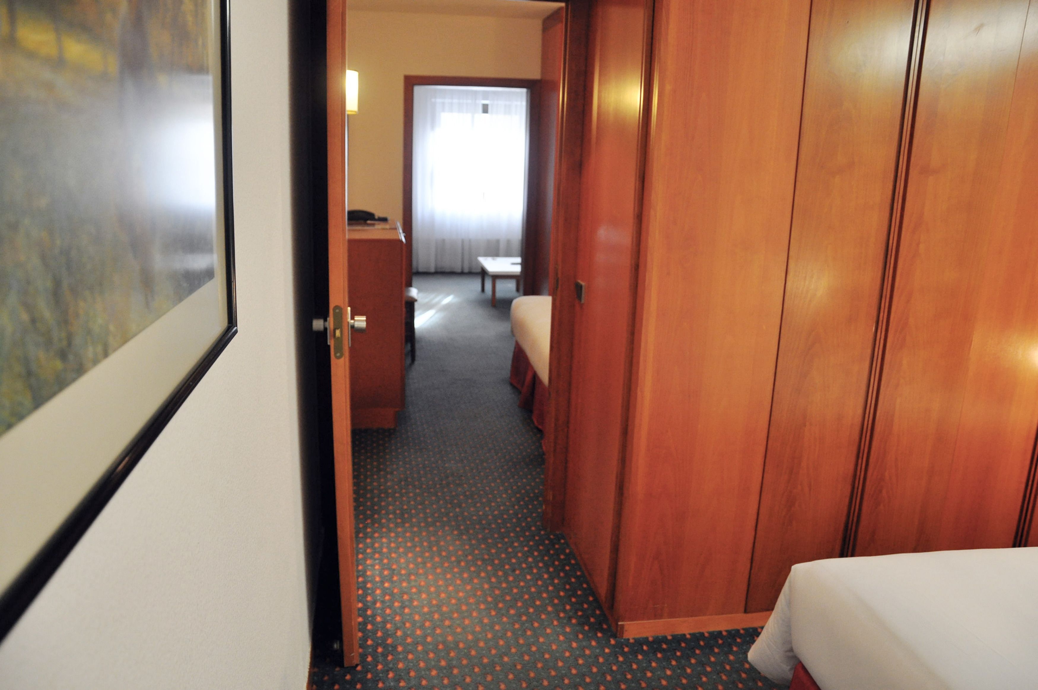 A hotel room with a bed, a wooden wardrobe, a desk, and a chair.