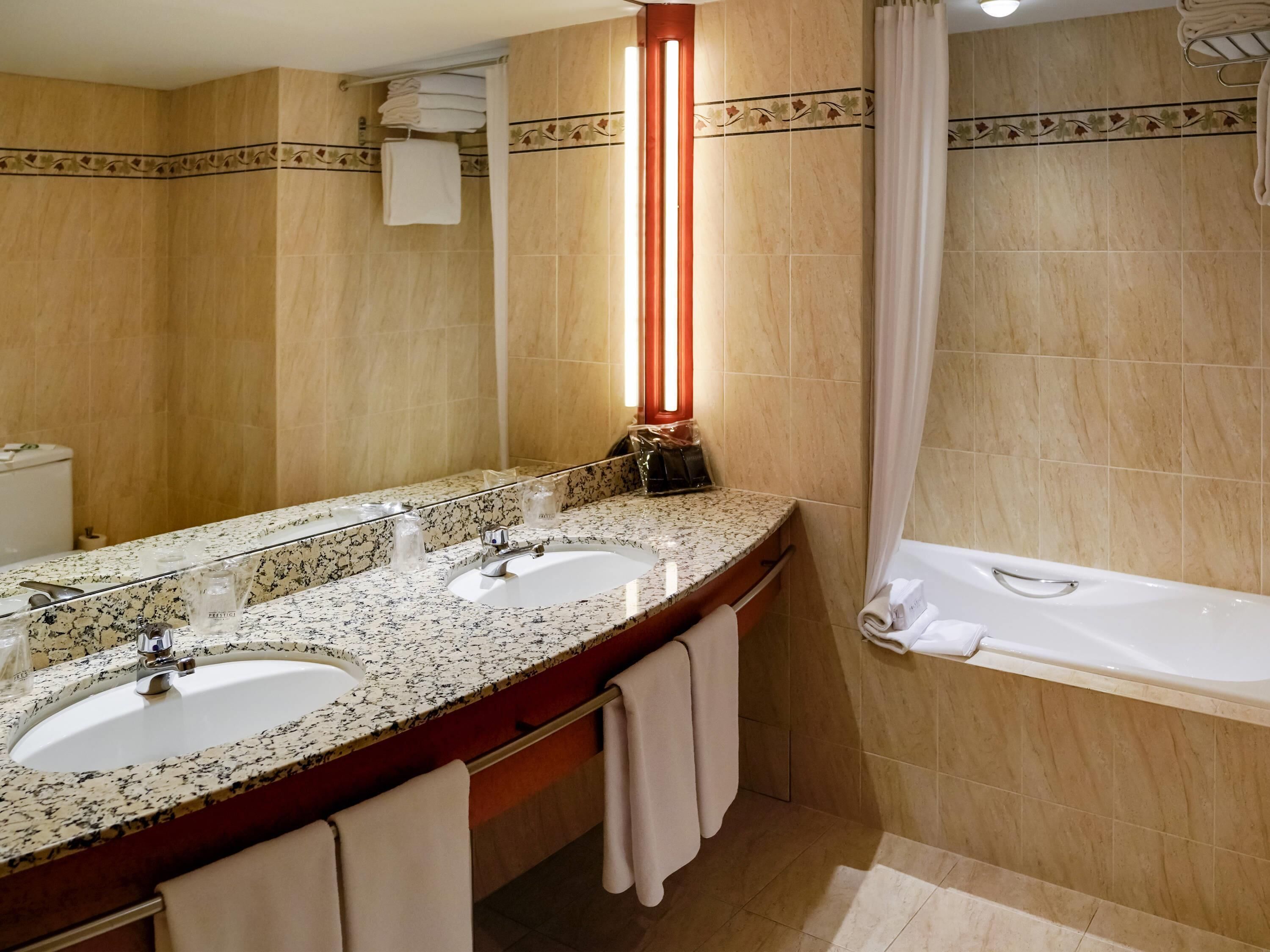 Un baño con dos lavamanos, un espejo grande, una bañera y un perchero para toallas.