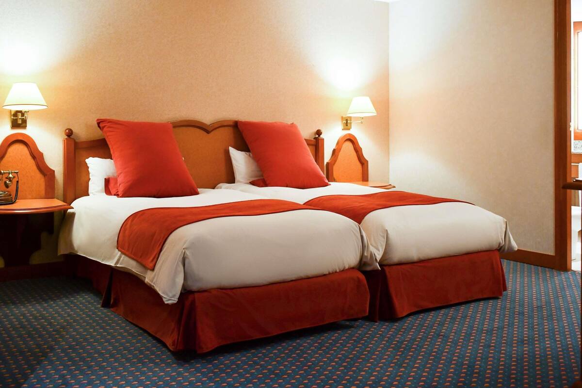 A hotel room with a double bed, two bedside lamps, a telephone, and a patterned carpet.