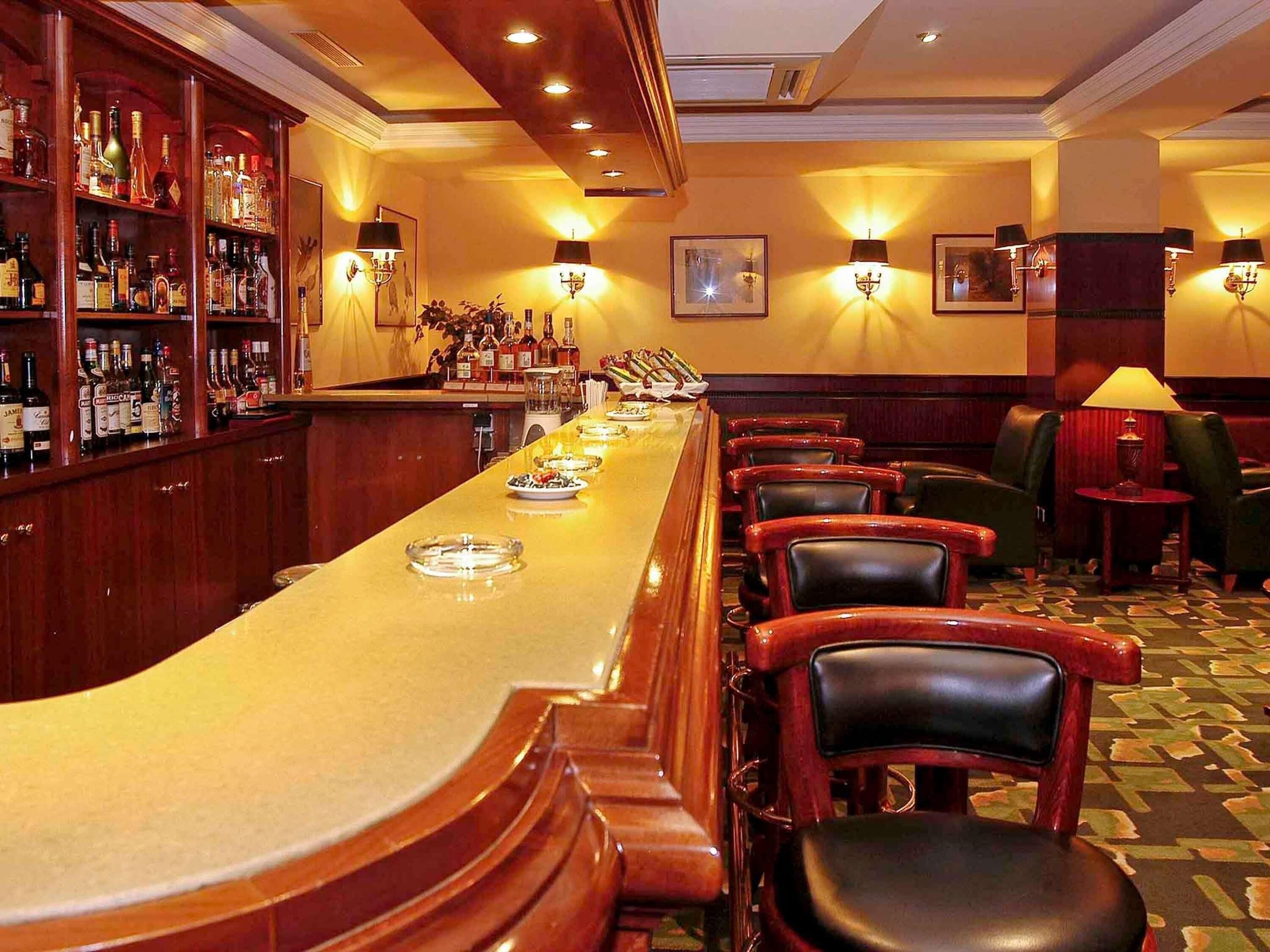 A bar area with a long counter, multiple chairs, and a bar stocked with liquor bottles.