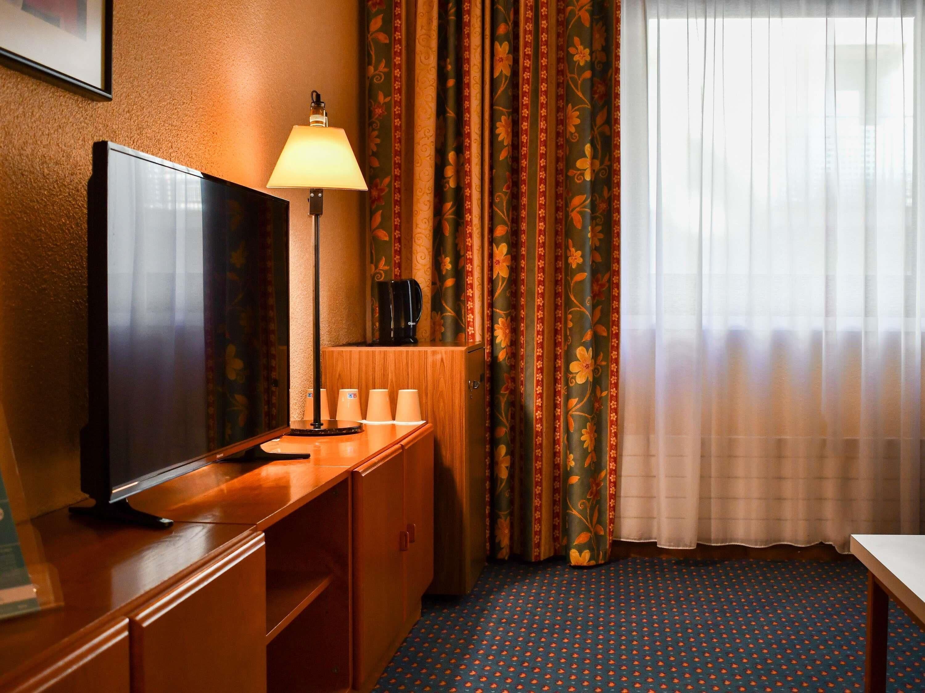 Una habitación de hotel con televisión, lámpara, cafetera y escritorio.