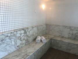 Un baño con paredes de azulejos blancos y escalones de mármol. Hay dos toallas enrolladas sobre los escalones.