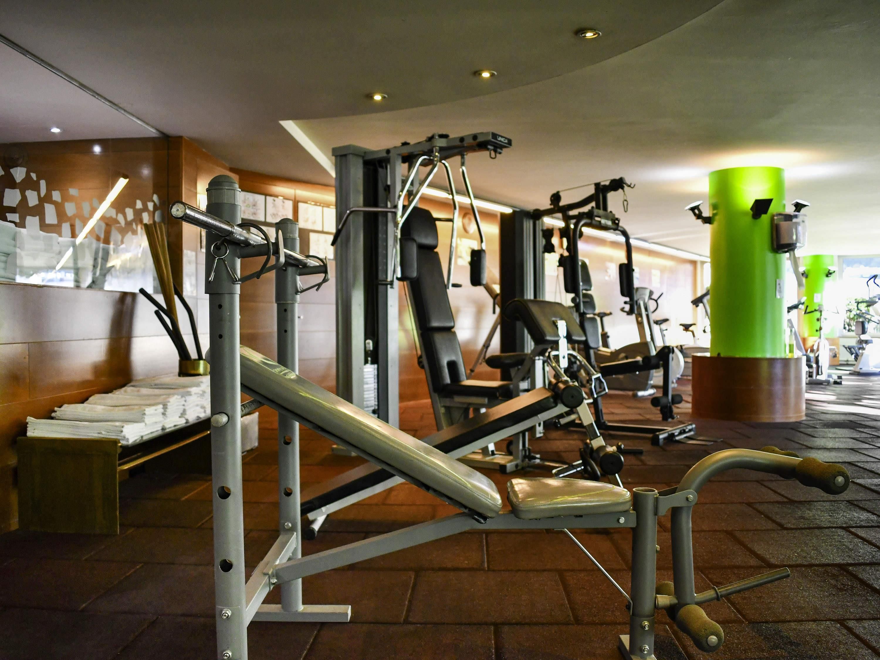 A gym with various exercise machines, a green pillar, and a tiled floor.