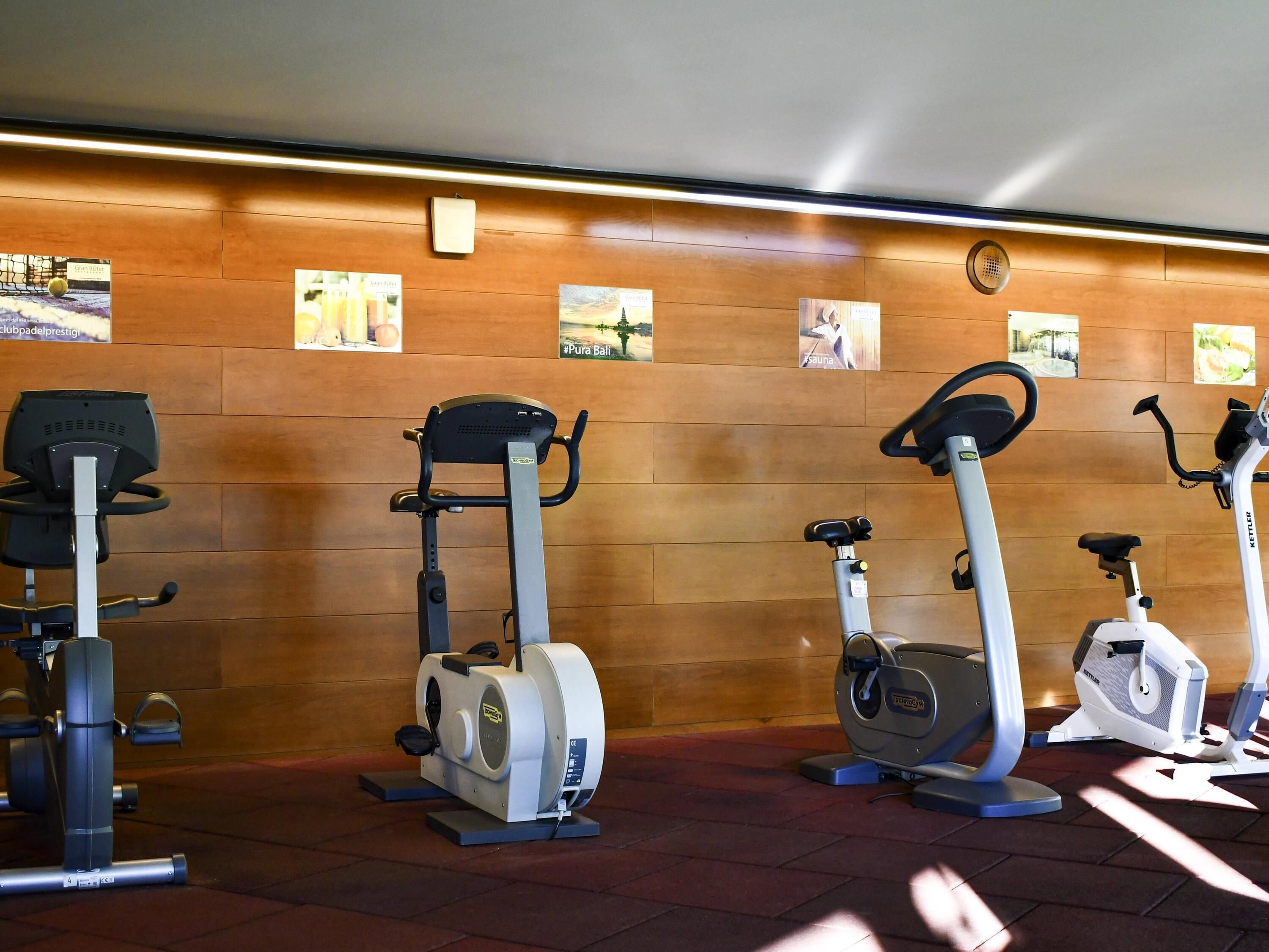 A gym with stationary bikes and ellipticals, wooden wall panels, and exercise posters.