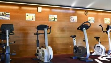 Un gimnasio con bicicletas estáticas y elípticas, paneles de pared de madera y carteles de ejercicios.
