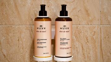 Dois produtos de cuidado capilar Nuxe em um dispensador fixado na parede.