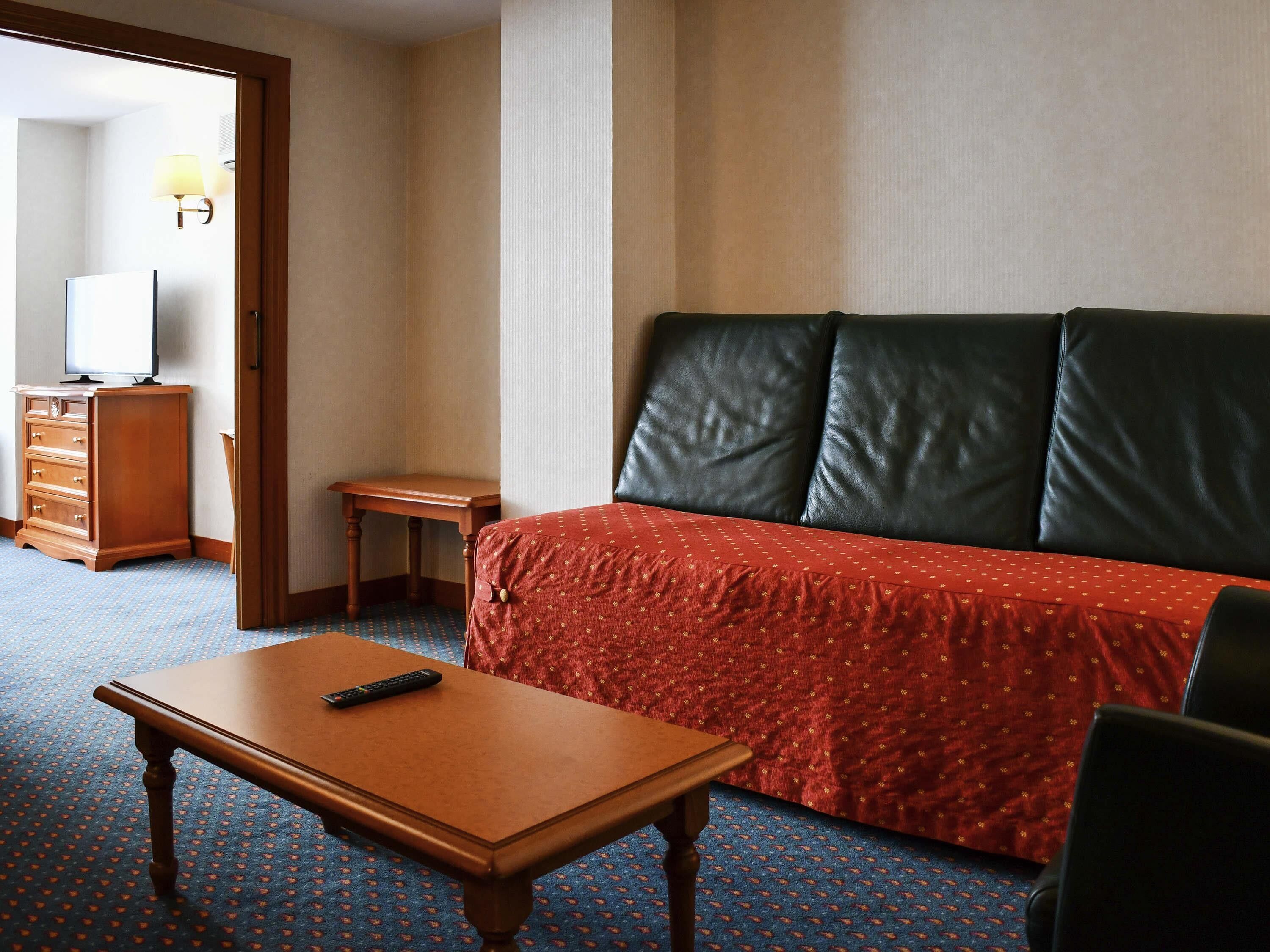 A hotel room with a bed, a wooden nightstand, a small table, and a television.