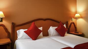 A hotel room with a double bed, two red pillows, a wooden headboard, two bedside tables, and wall-mounted lamps.