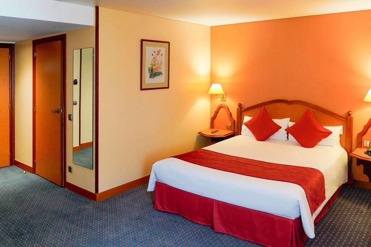 A hotel room with a large bed, two bedside tables, a nightstand, a mirror, and a door.