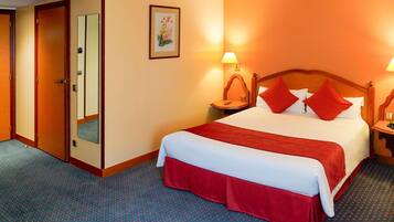 Una habitación de hotel con una cama grande, dos mesitas de noche, un tocador, un espejo y una puerta.