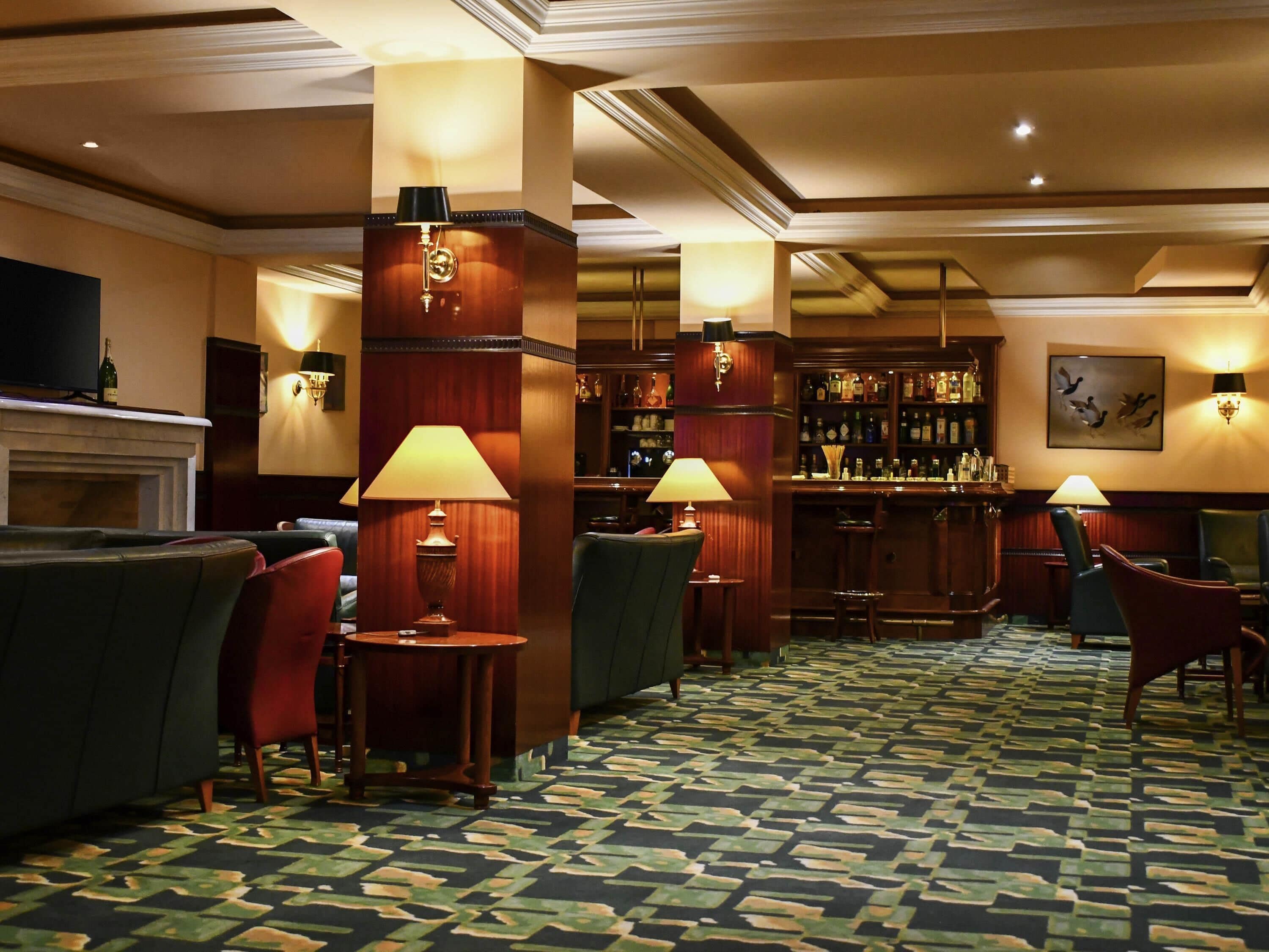 A bar area with wooden furniture, bar stools, and a patterned carpet.