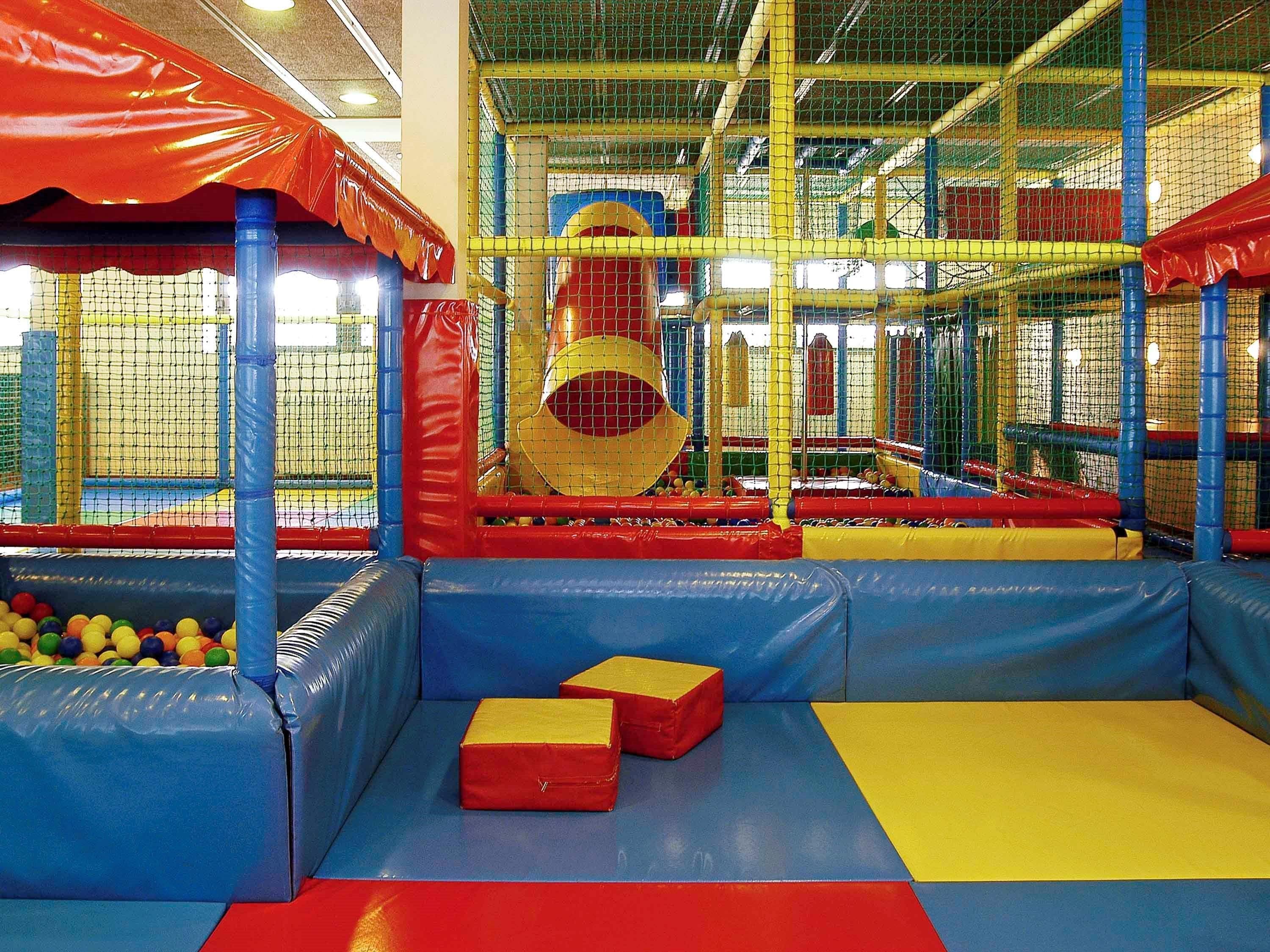 An indoor play area with padded play structures, a ball pit, and a climbing net.