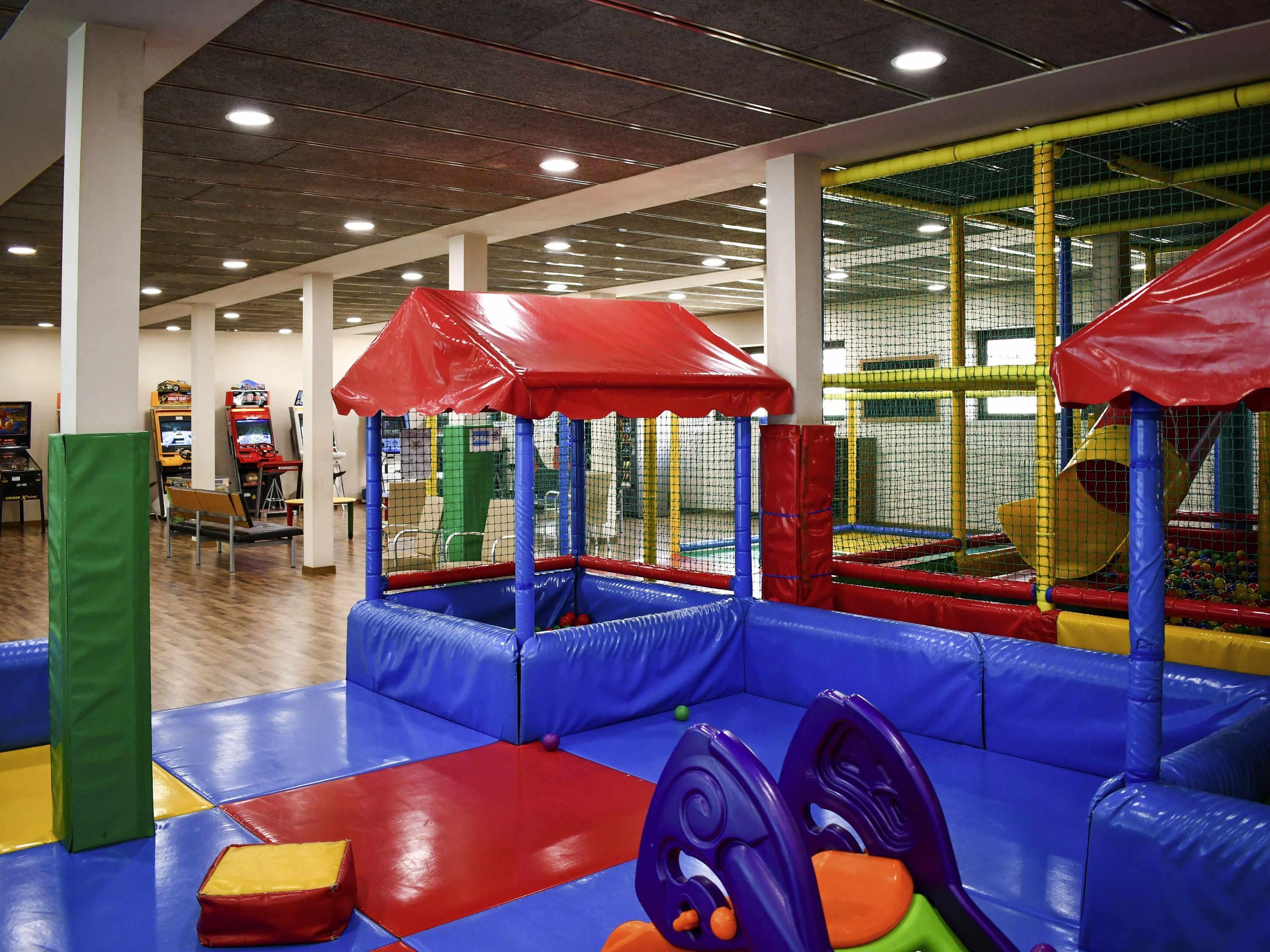 Un espace de jeux intérieur avec des structures de jeu rembourrées, une piscine à balles et des jeux d’arcade.