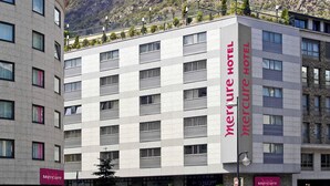 A Mercure Hotel with a modern design, featuring a prominent vertical sign, multiple windows, and a view of a mountainous landscape in the background. - Mercure Andorra (Andorra la Vella)