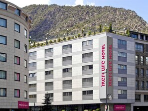 A Mercure Hotel with a modern design, featuring a prominent vertical sign, multiple windows, and a view of a mountainous landscape in the background. - Mercure Andorra (Andorra la Vella)