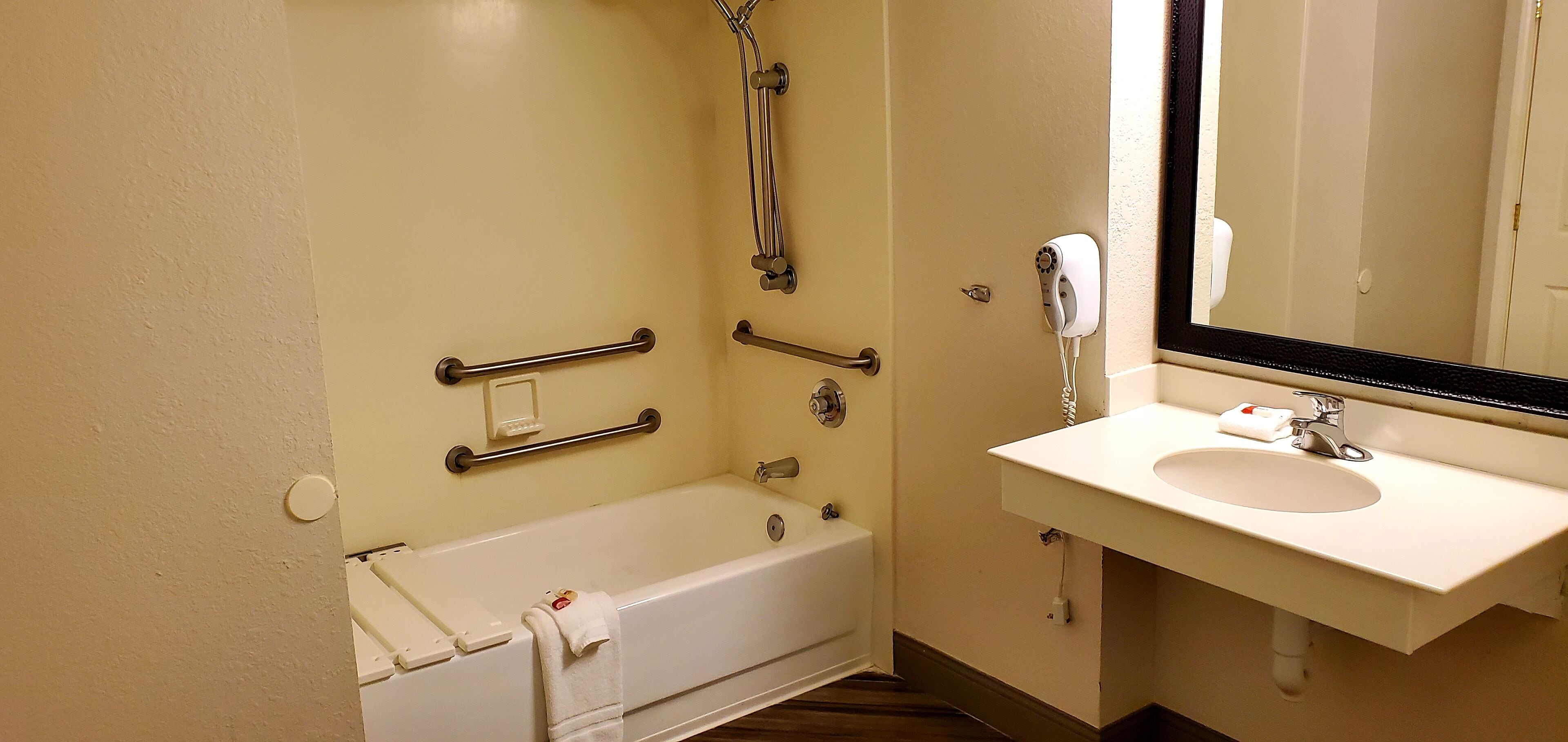 A bathroom with a bathtub, a handrail, a showerhead, a sink, and a mirror.