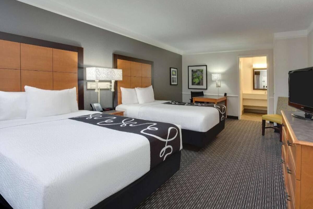 A hotel room with two beds, a desk, a chair, a television, and a lamp.