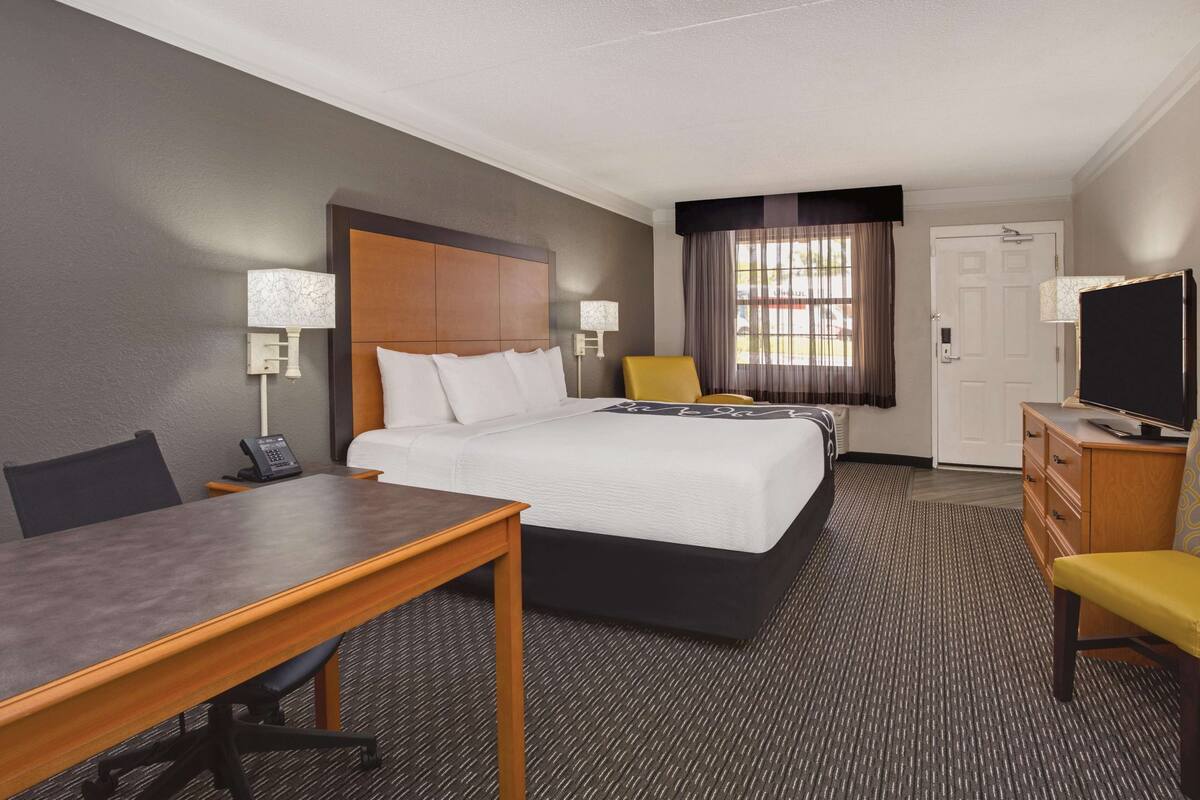 A hotel room with a bed, a desk, a chair, a television, and a window with curtains.