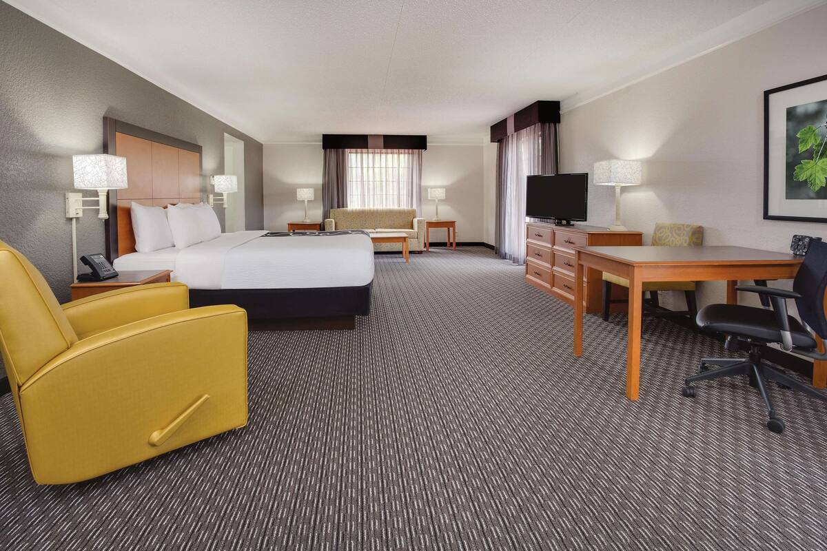 A hotel room with a large bed, a desk, a chair, a TV, and a telephone.