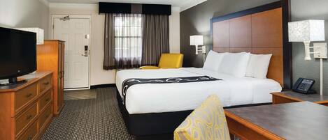 A hotel room with a bed, a television, a desk, a chair, and a window with curtains.