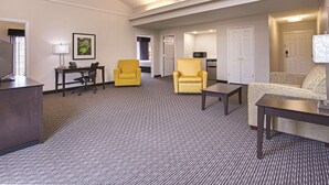 A hotel room with a carpeted floor, a desk with a lamp, two yellow armchairs, a sofa, and a television. - Days Inn by Wyndham Gainesville University I-75 (Gainesville)
