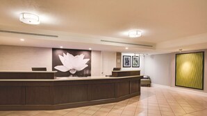 A reception area with a dark wooden reception desk, a large white floral wall art, and a tiled floor. - Days Inn by Wyndham Gainesville University I-75 (Gainesville)