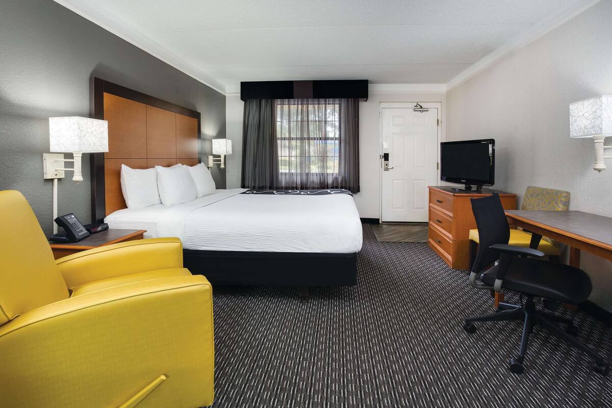 A hotel room with a bed, a desk, a chair, a television, and a telephone.