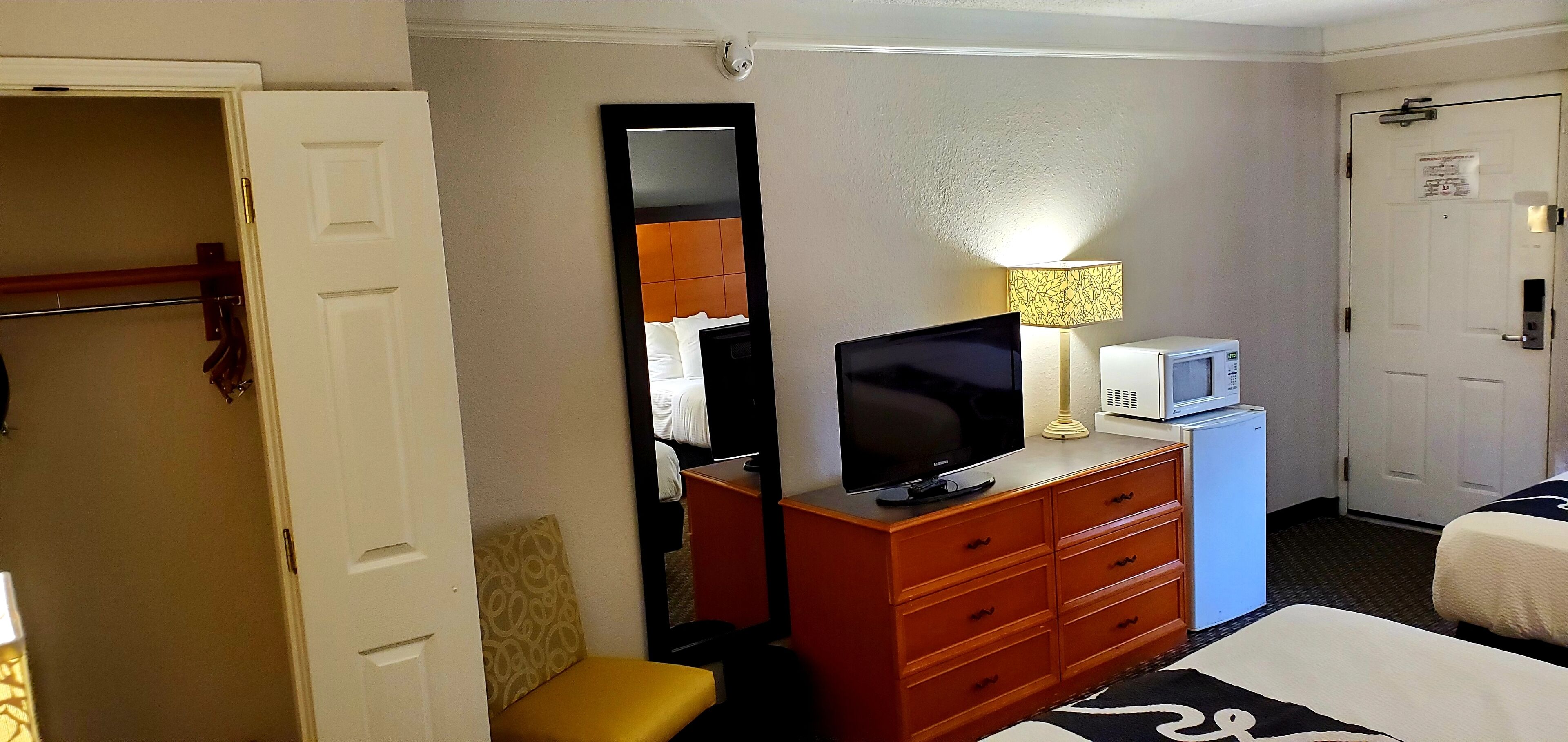 A hotel room with a bed, a television, a dresser, a mirror, a lamp, and a microwave.