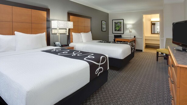 A hotel room with two beds, a desk, a chair, a television, and a bathroom visible through an open door. - Days Inn by Wyndham Gainesville University I-75 (Gainesville)