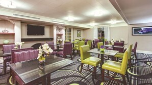 A hotel dining area with multiple tables and chairs, a flat-screen TV mounted on the wall, and a patterned carpet. - Days Inn by Wyndham Gainesville University I-75 (Gainesville)