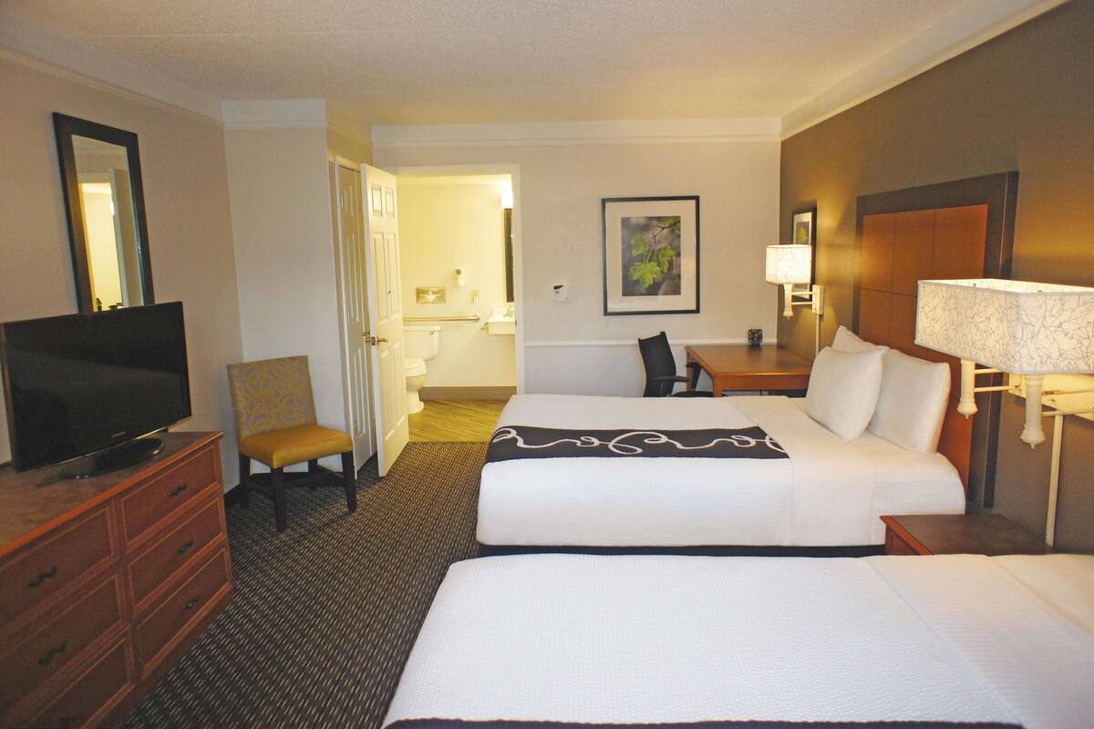 A hotel room with two beds, a television, a desk, and a chair.