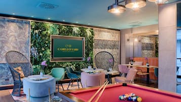 A billiards room with a pool table, green seating, and a wall with a 'Camelia's Yard' sign.