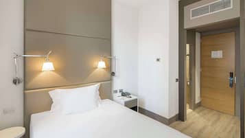 A hotel room with a large bed, two bedside lamps, a bedside table with a phone, and a wooden door.