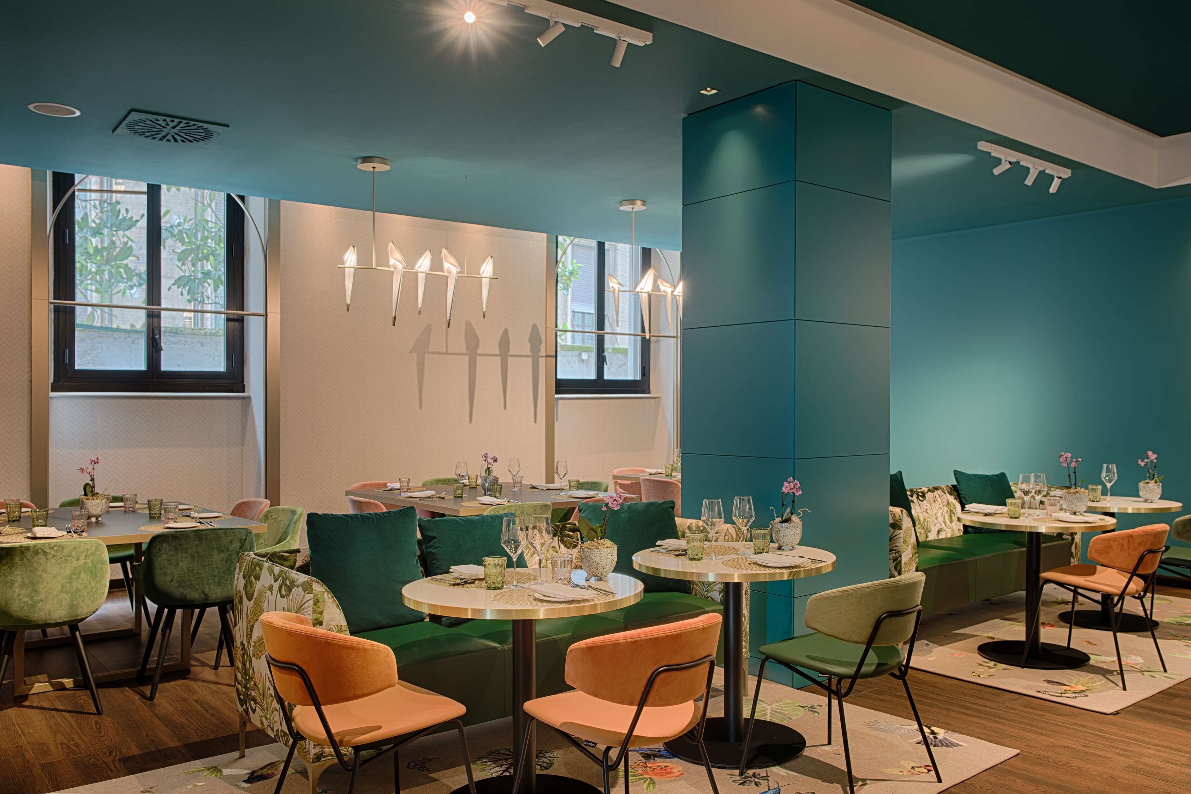A restaurant with round tables, green and orange chairs, and a teal-colored wall.